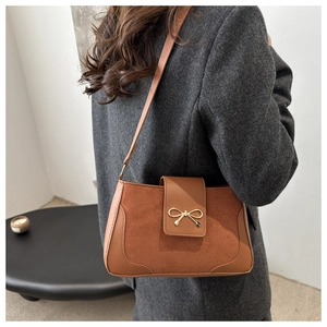 Close-up of brown suede and smooth leather shoulder bag with a gold bow clasp