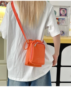 Detail of bright orange nylon crossbody bag with drawstring closure worn by a model