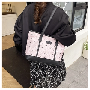 Detail of pink pleated tote bag with black bow prints and logo tag on a female model