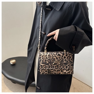 Detailansicht der Leoparden-Handtasche mit goldener Schleifenschnalle auf schwarzem Mantel