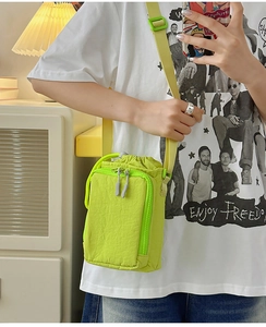 Detail of lime green nylon crossbody bag with drawstring closure and grey zippers