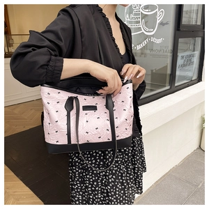 Close-up of pink tote bag featuring black bow prints and leather shoulder straps