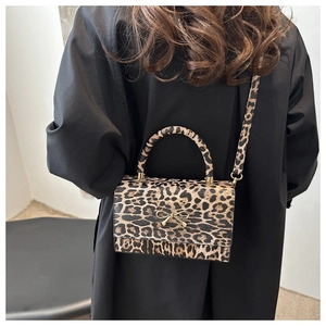 Detail der Handtasche mit Leopardenmuster und goldener Schleife an Modell im schwarzen Mantel