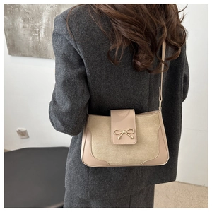 Detail of beige shoulder bag featuring mixed leather texture and golden bow ornament