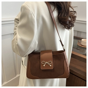 Detail of a dark brown crossbody bag with suede stitching and a golden bow lock