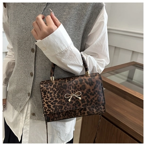 Detail of leopard print handbag with golden bow buckle on model with grey vest