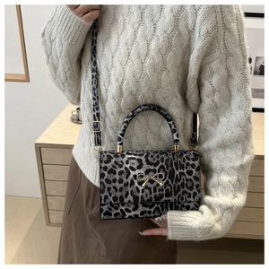 Detail of leopard print handbag with golden bow clasp on white knit sweater