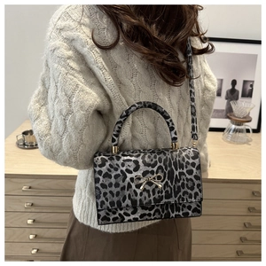 Detail of leopard print handbag with gold bow hardware on a textured winter outfit