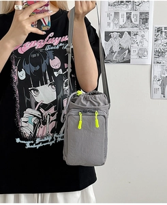 Gray nylon crossbody bag with neon yellow zipper pull worn on a street style model