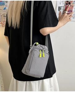 Detail of grey nylon crossbody bag featuring neon yellow zipper and drawstring design