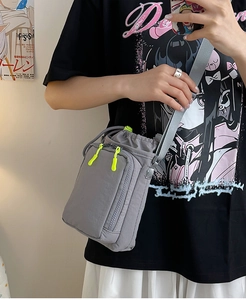 Detailed mirror selfie showing a grey nylon crossbody bag with neon yellow zipper pullers