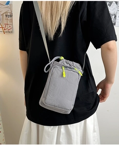 Detail of grey crossbody mini bag with vibrant neon green drawstring zipper on fabric