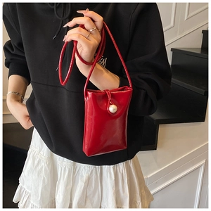 Detail of red glossy mini phone bag with a large pearl buckle on a slim shoulder strap