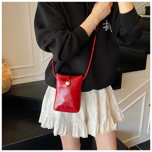 Detail of red patent leather mini phone bag with white pearl buckle and thin strap