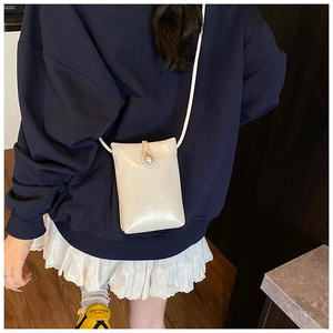 Close-up of cream mini phone bag with pearl buckle and smooth faux leather texture
