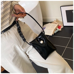 Detail view of mini black patent leather bag with large pearl button and chunky chain strap