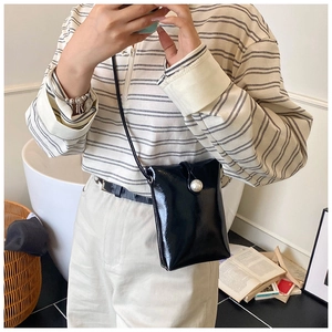 Detail of a minimalist black shiny crossbody phone bag with a large pearl buckle decoration