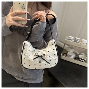 Detail of white seersucker hobo bag with black bows and heart charm held by a model