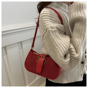 Detail of red suede shoulder bag with vintage golden buckle worn over a beige sweater