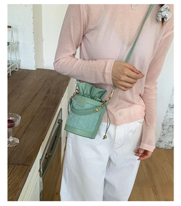 Detail view of light green drawstring bucket bag with woven texture and leather strap