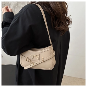 Detail of beige shoulder bag featuring a decorative gold bow buckle and leather strap