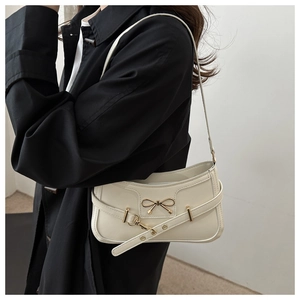 Détail d'un sac sous le bras blanc crème avec un nœud métallique et une sangle décorative