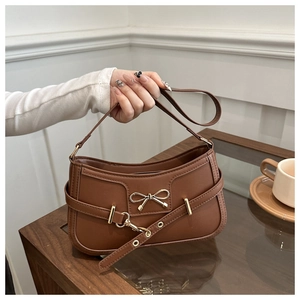 Détails d'un sac en cuir marron avec nœud doré et lanières croisées décoratives