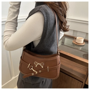 Close-up of vintage brown baguette bag with golden bow lock and eyelet strap detail