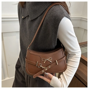 Détail d'un sac porté épaule marron vintage avec nœud doré porté par un modèle