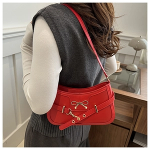 Sac bandoulière en cuir rouge avec boucle dorée porté par un mannequin dans un salon