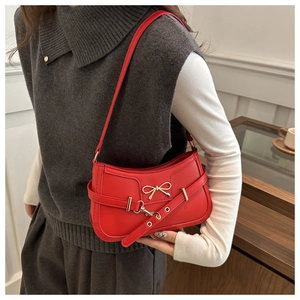 Détail du sac croissant rouge avec nœud doré et bandoulière à œillets ajustables