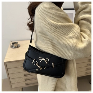 Close-up of black shoulder bag with gold butterfly hardware on cream knitted sweater