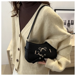 Détail du sac baguette noir avec nœud doré et fine sangle en cuir à boucle métallique