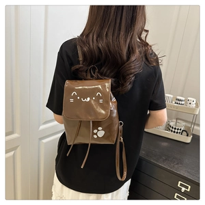 Brown patent leather mini backpack with cat graphics shown on a model in a home setting
