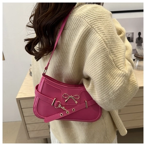 Détail du sac sous l'aisselle rose avec nœud doré et bandoulière à boucle sur modèle
