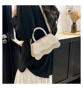 Dettaglio borsa a tracolla beige con fiocco dorato e bordo ondulato elegante