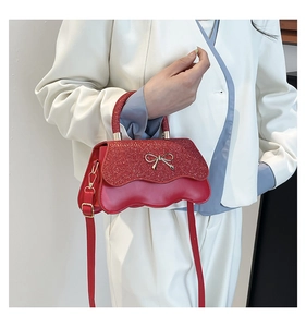 Dettaglio borsa a tracolla rossa glitterata con patta a onde e fiocco dorato