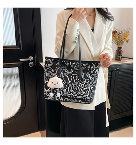Detail of a black tote bag with white graffiti patterns and a plush cloud charm