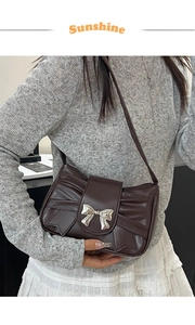Détail d'un sac à bandoulière plissé marron foncé avec une boucle décorative en nœud doré