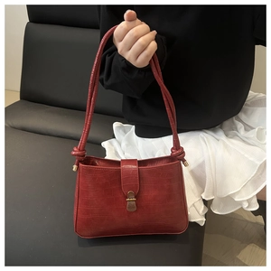Detail of burgundy crocodile pattern leather bag featuring a gold clasp and knot strap