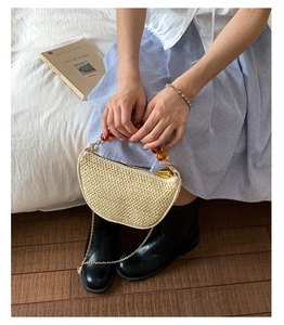 Detail of cream woven half-moon bag with amber bead handle and sleek metal chain
