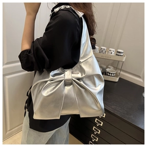 Detail shot of the large silver bow design and metallic leather texture on the shoulder bag