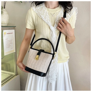 Detail of woven straw bucket bag with black leather trim and gold hardware accents