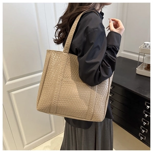 Chic beige woven tote bag shown on shoulder in a minimalist indoor setting