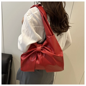 Detail view of a large red bow tote bag shown on a shoulder in minimalist indoor setting