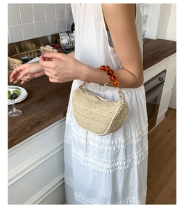Detailed straw weave texture of cream half-moon bag with amber beaded handle