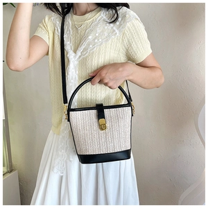 Detail of woven straw bucket bag with black leather trim and golden metal turn-lock
