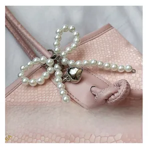 Close-up of white pearl bow pendant with silver heart charm on pink snakeskin bag