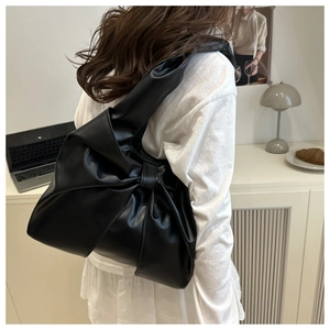 Side view of black matte leather shoulder bag with large bow and wide strap on model