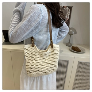 Dettaglio borsa beige intrecciata a mano con tracolla in pelle marrone e rivetti su modella